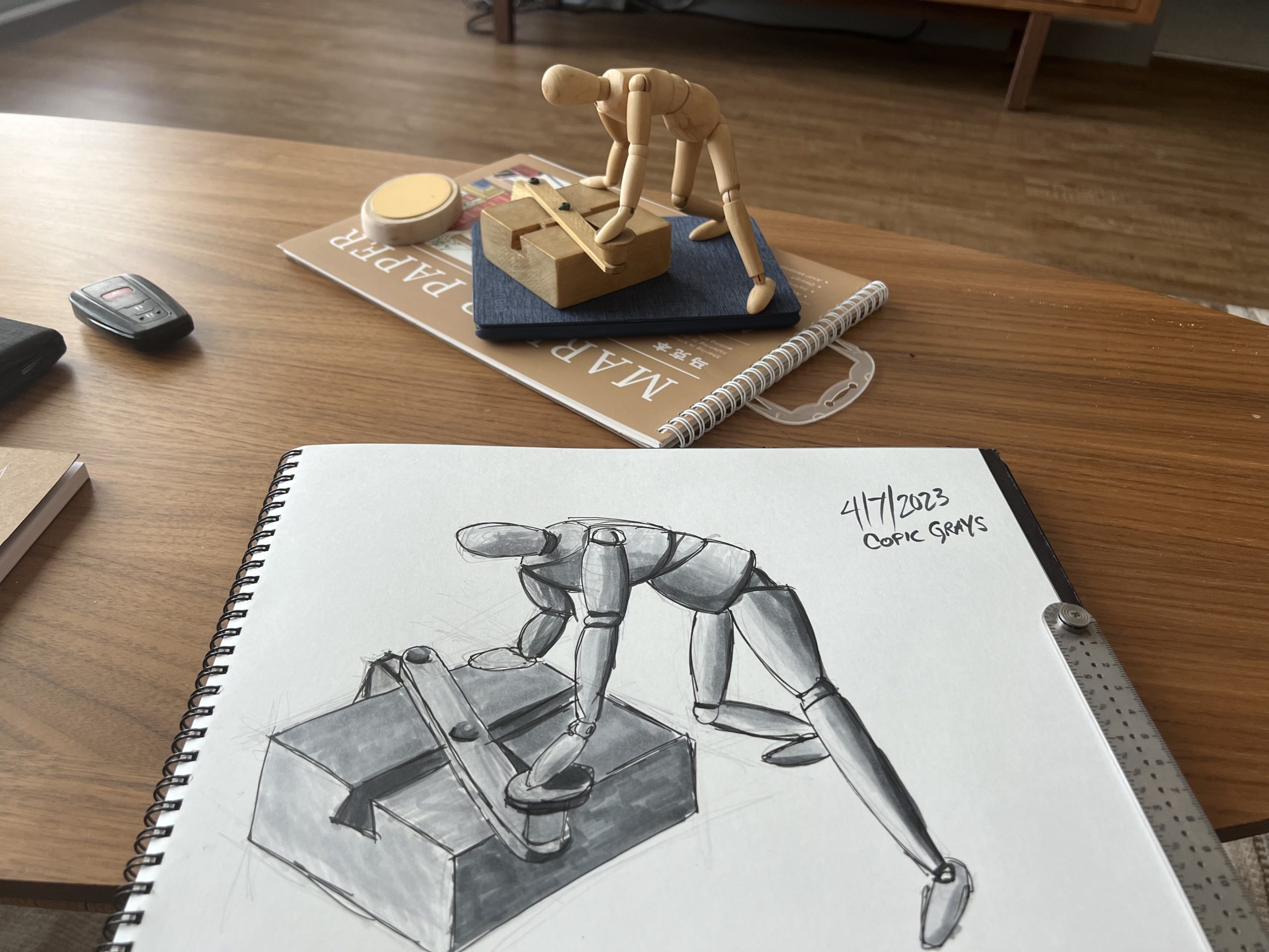 A sketch of a small wooden figure with a wooden do nothing machine (in front of the actual figure and machine)